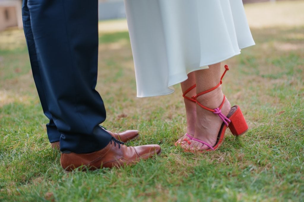 Hochzeitspaar mit Fokus auf Schuhe und Kleidung, romantische Atmosphäre im Freien.