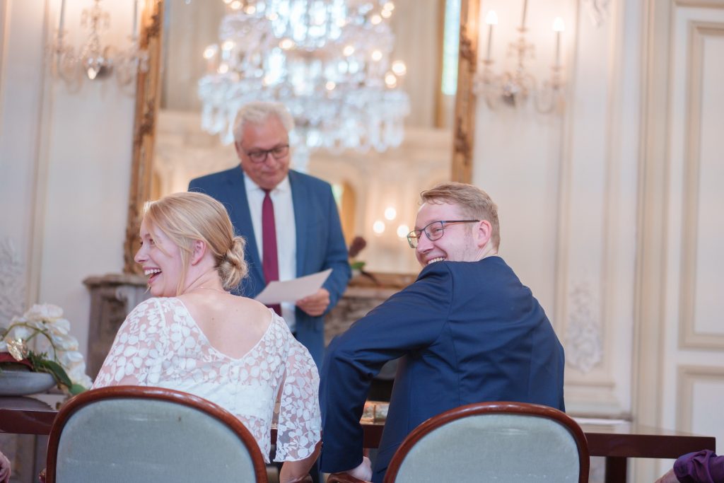 Hochzeitspaar bei Trauung im eleganten Saal, lachend und glücklich, mit Hochzeitsfotografie von Alis.